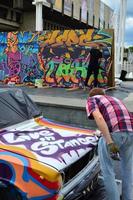 KHARKOV, UKRAINE - MAY 27, 2017 Festival of street art. Young guys draw graffiti on the car body in the city center. The process of drawing color graffiti on a car with aerosol cans photo