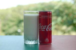KHARKOV. UKRAINE - MAY 2, 2019 Coca cola red tin can and cup of fresh milk on colored surface photo