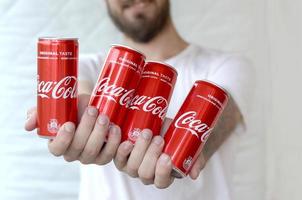 Jarkov. ucrania - 2 de mayo de 2019 hombre sonriente sosteniendo muchas latas de aluminio de coca-cola sin alcohol en el interior del garaje foto