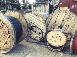 Madejas redondas de madera con cable eléctrico. el cable se enrolla en un carrete grande de madera. cerca de contenedores metálicos de basura para recoger residuos grandes foto