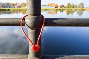 A red barn lock in the shape of a heart hangs on the railing of a bridge. Wedding tradition to hang locks on bridges for eternal love photo