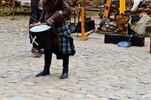 un guerrero escocés, soldado, músico con traje tradicional con falda toca el tambor en la plaza de un antiguo castillo medieval. foto