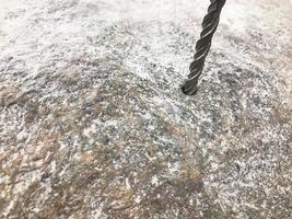 una broca de metal duro y resistente perfora un agujero en una gran piedra gris. cerrar vista el fondo foto