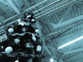 Festive green beautiful elegant Christmas tree with balls for the New Year on the background of the ceiling with metal ventilation pipes in the loft style. Concept Christmas at an industrial plant photo