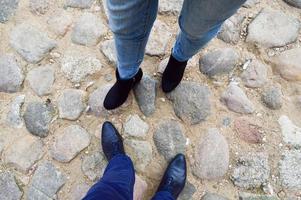 piernas masculinas y femeninas en zapatos de cuero, botas en un camino de piedra de grandes adoquines uno frente al otro. el fondo
