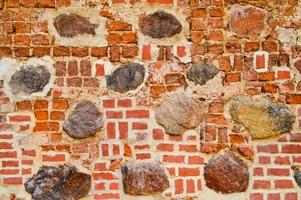 The texture of the old ancient medieval antique stone hard peeling cracked brick wall of rectangular red clay bricks and large stones, cobblestones. The background photo