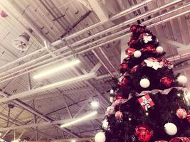 Festive green beautiful elegant Christmas tree with balls for the New Year on the background of the ceiling with metal ventilation pipes in the loft style. Concept Christmas at an industrial plant photo