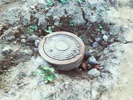 hatch at a construction site. metal hatch cover, volumetric, silver, dug into the ground. hatch to protect groundwater. sewerage drainage. stones and dirt next to the hatch photo