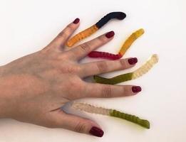 long, mouth-watering, multi-colored worms on the hand of a girl with a bright red manicure. the worms lie between the fingers. unusual creative shooting. volumetric structure, dessert photo