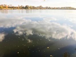 hermoso paisaje otoñal con árboles y hojas amarillas en el lago contra el cielo azul en un día soleado foto