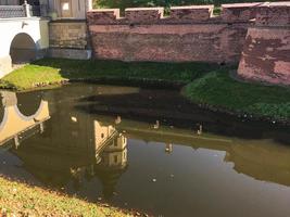 A large red brick earthen wall is strong protective and a moat with the war of an old, ancient medieval castle in the center of Europe and river with water photo