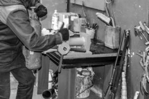 A male worker on a large metal industrial vice is repairing a red fire extinguisher cylinder in a workshop at the plant photo