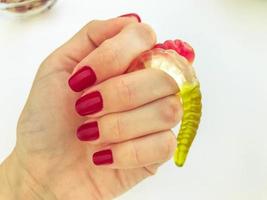 a lot of gummy worms lie with a girl with a red manicure on an orange matte background. delicious appetizing dessert. handmade worms photo