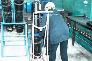 A worker in a helmet is loading a gas oxygen cylinder onto a trolley at an industrial plant photo