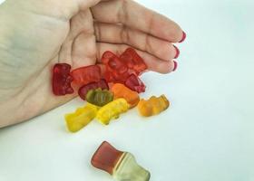 gummy candy on a white matte background. jujube closes girl with red manicure. the girl hides her candies from everyone. gelatinous sweet candies in the shape of bears photo