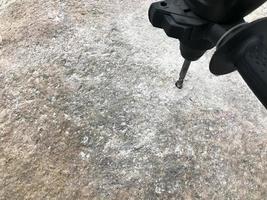 A sturdy, hard metal iron drill bit drills a hole in a large gray stone. Close view. The background photo