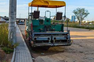 máquina pavimentadora de asfalto de dos plazas, coche abierto con toldo y techo de tela amarilla. la cuchara de pavimentación de asfalto está instalada en la parte trasera. construcción de un nuevo complejo foto