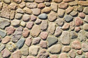 The texture of the stone road, pavement, walls of large gray old medieval round strong stones, cobblestones. The background photo