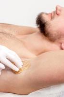 Cosmetologist applying wax paste on male armpit photo