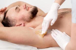 Cosmetologist applying wax paste on male armpit photo