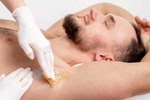 Cosmetologist applying wax paste on male armpit photo