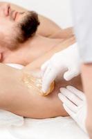 Cosmetologist applying wax paste on male armpit photo