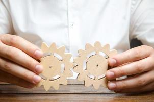 Businessman in white shirt connects two wooden gears. Symbolism of establishing business processes and communication. Improving work efficiency, establishing new connections and suppliers. photo