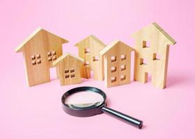 Many wooden figures of houses and a magnifying glass. Search for housing to buy or rent, realtor services. Find the best real estate option. Criteria and advice for making the right choice. photo