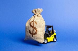 Yellow forklift truck carries a big bag of money. Attracting investment in the development and modernization of production and business projects. Revenue, profit, sales. super profit. copy space photo