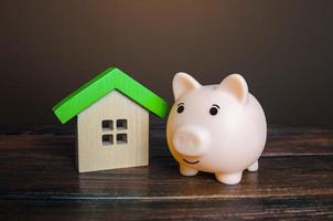 Piggy bank near a house. Savings on household bills, energy saving technologies. Save up for a new house. Mortgage loan. Maintenance, property improvement. Real estate market. Buying or selling. photo