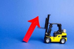 A yellow forklift raises a big red arrow up. Growth in production rates and development of industry and infrastructure. Increased sales, economy growth. Concept of increase, growth and success. photo
