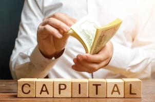 Businessman counts money on the background of the caption Capital. Capitalism, capital increase and influence. Financial liberalization of developing countries, unprincipled withdrawal of capital. photo