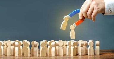 Businessman with a magnet pulls wooden figures of people out of big crowd. Recruiting workers. Search for required people and workers with the necessary talents and skills.. Formation of a new team photo