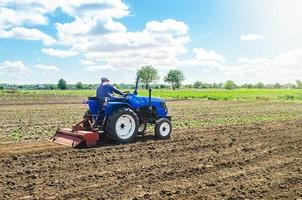 A farmer on a tractor mills the soil with a milling machine equipment. Grinding loosening soil, removing plants and roots from last harvest. Growing vegetables. Ground crumbling and mixing. photo