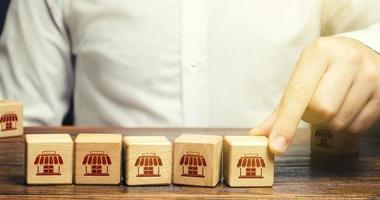 el hombre pone bloques con símbolos de tienda en una fila. construyendo un imperio empresarial exitoso. concepto de franquicia. competidor de fusión, creación de un gran monopolio de la red. asociación comercial foto