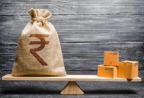 Indian rupee INR symbol money bag and a bunch of boxes on scales. Trade exchange balance. Import and export, economic processes. Profit from manufactured goods. Manufacturing, retail distribution photo