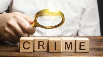 Man with a magnifying glass examines the word Crime. Investigation. Collection evidence, identification of perpetrators, familiarization with court case. Detective, criminal forensic expert. Expertise photo