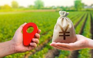 Hands with location pin and chinese yuan or japanese yen money bag. Land market. Buying and selling land. Estimation cost of plots. Agriculture agribusiness. Transport and construction industry. photo