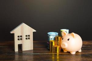 Piggy bank and coins near a house. Savings on home bills, energy saving technologies. Save money to buy a new house. Maintenance, property improvement. Real estate market. Mortgage loan.