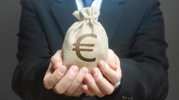 A man holds out a euro money bag. Granting financing business project or education. Provision cash financial loan credit. Investment. Bank deposit. Budget management, tax collection. Trade, economics. photo