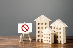 Figures of residential buildings and red prohibition sign no. Inaccessible and expensive housing. Seizure and freezing of assets by a bank, court. Restrictions and a ban on the construction of housing photo