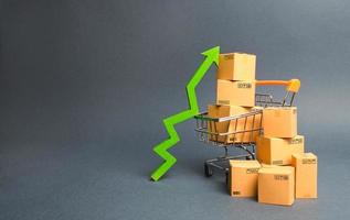Shopping cart with cardboard boxes and a green up arrow. Increase the pace of sales and production of goods. Improving consumer sentiment, economic growth. Strategy for increasing revenue photo