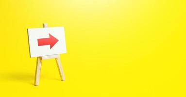 Easel with a red right arrow on a yellow background. Sign of direction. Advertising of the location of a store or outlet. Minimalism. Restriction of movement. Short road.