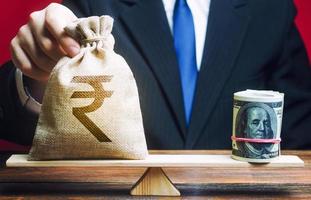 Businessman puts indian rupee money bag on the scales opposite to the dollar roll. Exchange rate, comparison of economic indicators. Avoiding savings inflation. Investments in foreign currency bonds. photo