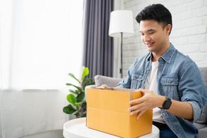 Unpacking parcel. Happy Asian male customer sits on the sofa at home and unpacks the parcel at home. Delivery service concept. photo