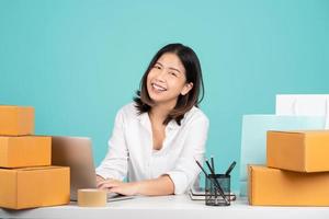 Asian businesswoman in a casual shirt sits at her desk with a brown cardboard box. She is using the internet online. Isolated on a green background. photo