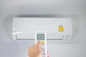 Closeup of an Asian hand holding a remote control of an air conditioner on a white wall. Turn on the air conditioner. photo