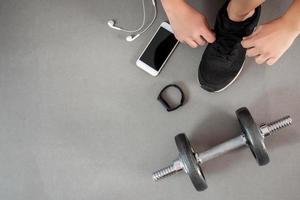 The top view of a man's hand wearing a shoelace in the gym with a smartphone, a smart watch and a dumbbell. photo