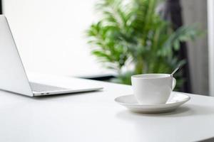 primer plano de una taza de café caliente para un joven hombre de negocios en un escritorio blanco con sol matutino en casa. foto