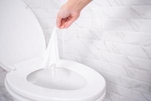 Close up hand throwing toilet paper to the toilet in a white tile bathroom photo